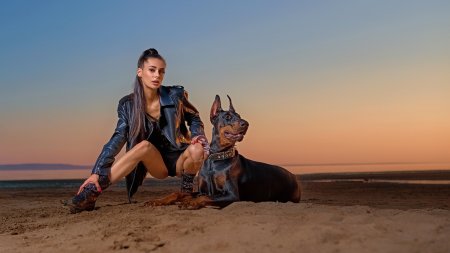Brunette girl posing on the shore with a Doberman